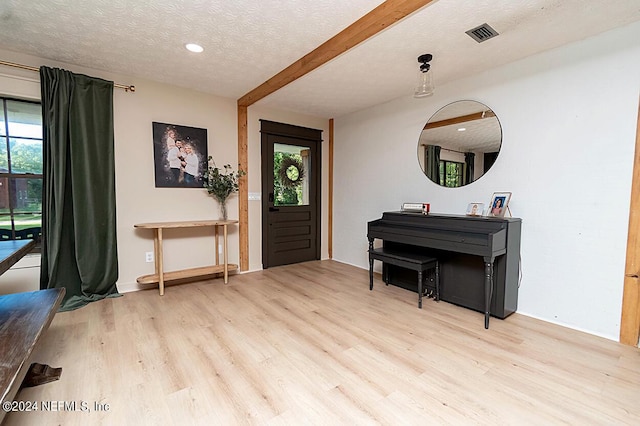 foyer entrance featuring beam ceiling, a textured ceiling, and light hardwood / wood-style flooring