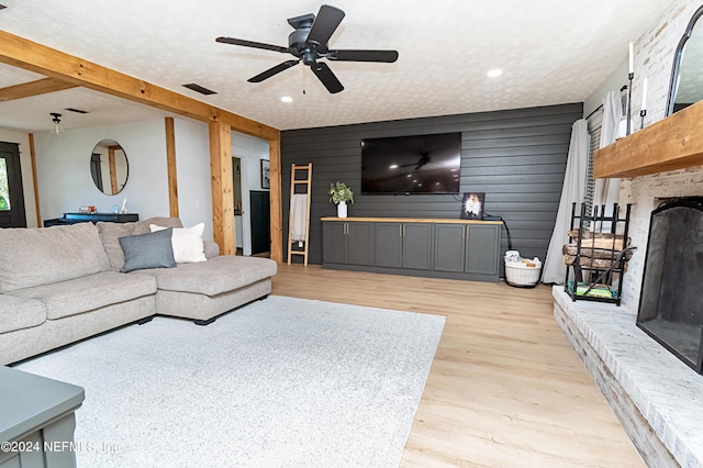 living room with a textured ceiling, beamed ceiling, wooden walls, light wood-type flooring, and ceiling fan