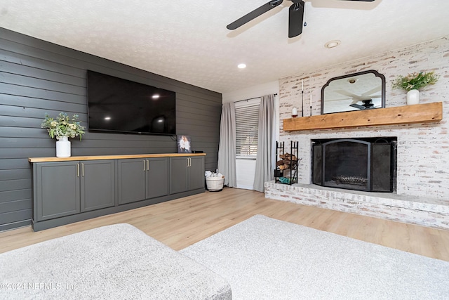 living room with a textured ceiling, a fireplace, wood walls, ceiling fan, and light hardwood / wood-style flooring