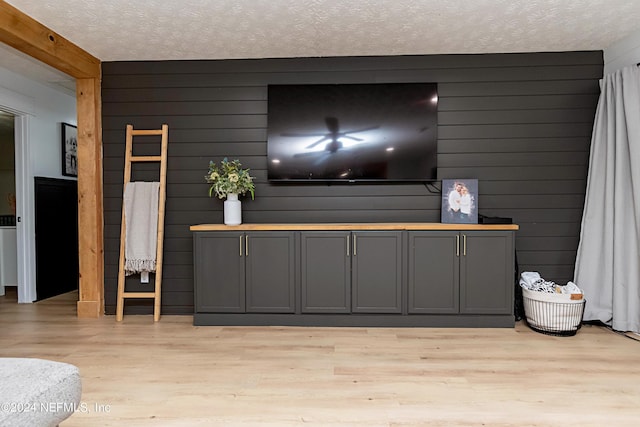 living room with a textured ceiling, light hardwood / wood-style flooring, and wood walls