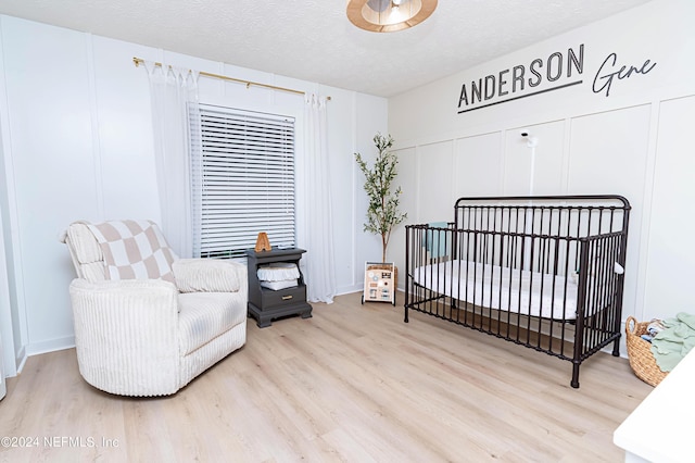 bedroom featuring a textured ceiling, a nursery area, and light hardwood / wood-style flooring