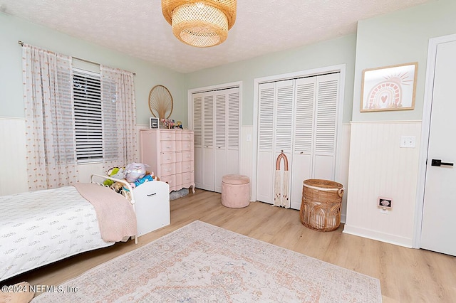 bedroom with two closets, a textured ceiling, and light hardwood / wood-style flooring