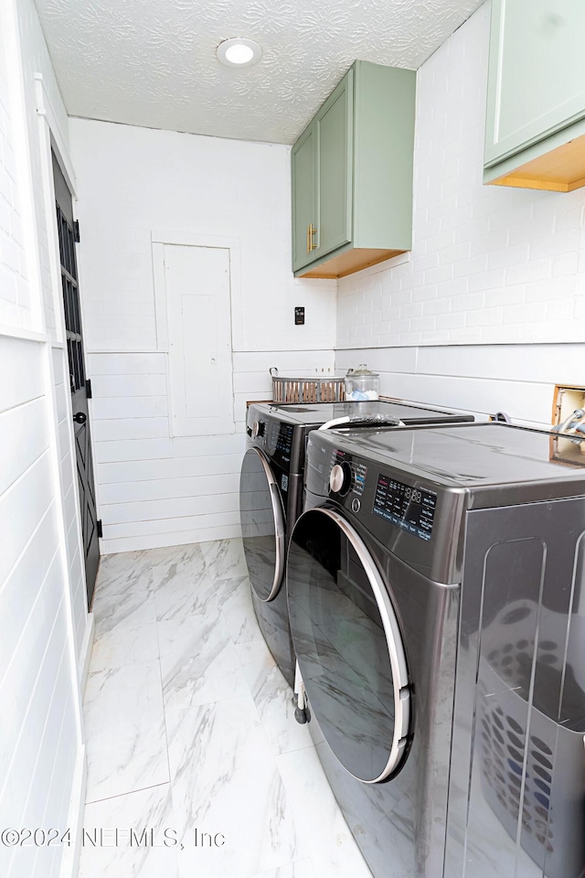 clothes washing area with washer and dryer, cabinets, and a textured ceiling