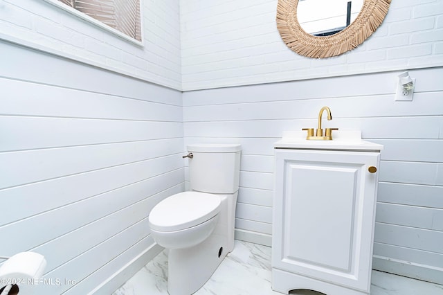 bathroom featuring toilet, vanity, and wood walls