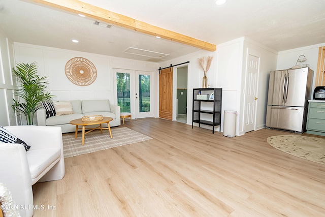 living room featuring beam ceiling, a barn door, and light hardwood / wood-style floors