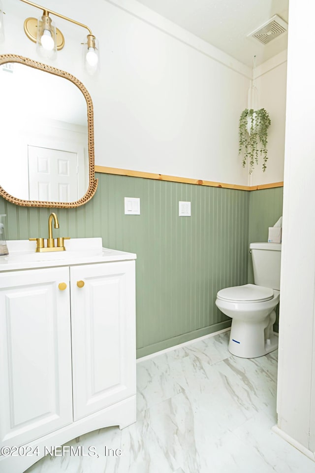 bathroom featuring toilet, vanity, and wooden walls