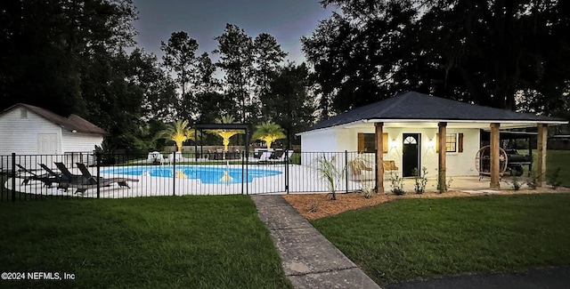 pool at dusk featuring an outbuilding, a patio area, and a yard