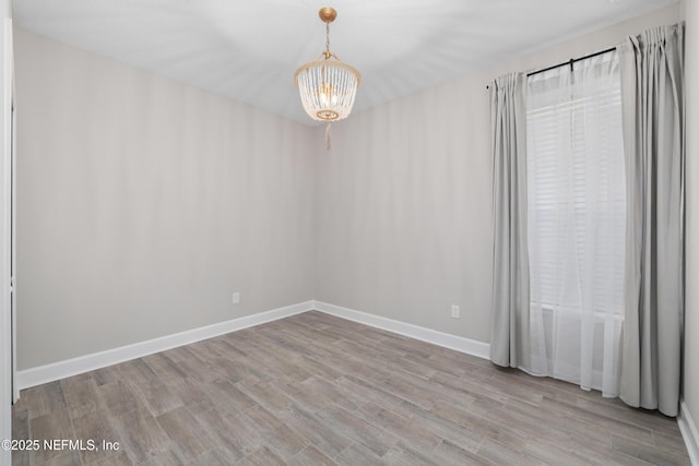 unfurnished room with a chandelier and light wood-type flooring