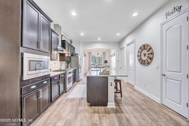 kitchen with a breakfast bar, backsplash, stainless steel appliances, light stone countertops, and a center island with sink