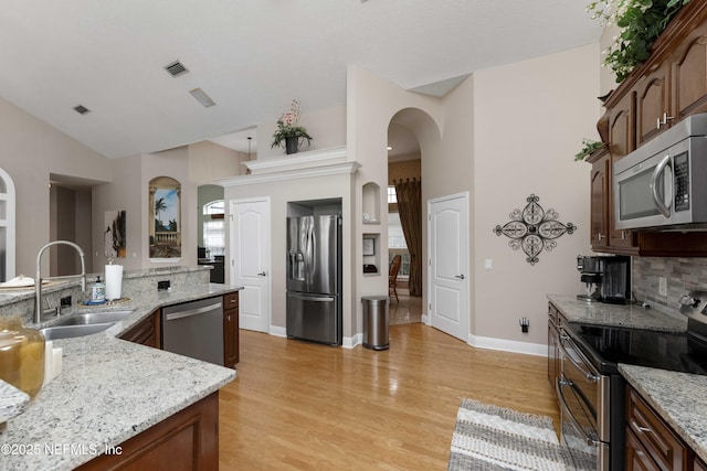 kitchen with light wood-type flooring, light stone countertops, appliances with stainless steel finishes, and sink