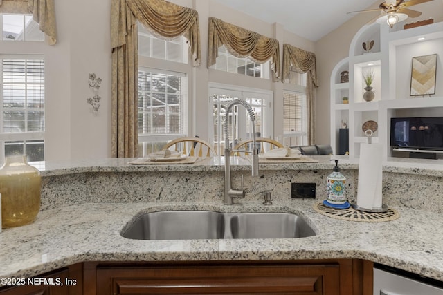 kitchen with ceiling fan, sink, built in features, and light stone countertops