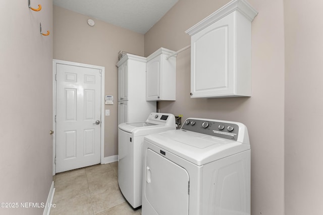 laundry area with light tile patterned floors, independent washer and dryer, a textured ceiling, and cabinets