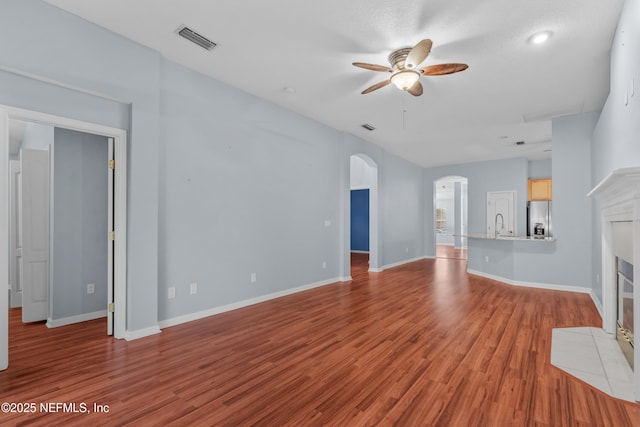 unfurnished living room featuring ceiling fan, a fireplace, sink, and light wood-type flooring