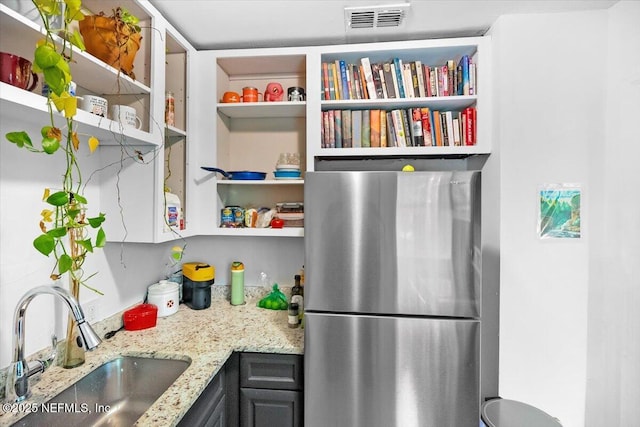 kitchen featuring light stone countertops, sink, and stainless steel refrigerator