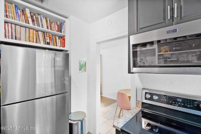 kitchen featuring gray cabinets, appliances with stainless steel finishes, light tile patterned floors, and light stone counters