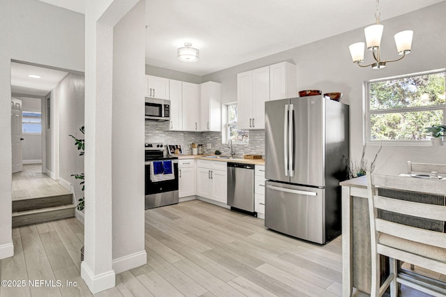 kitchen with appliances with stainless steel finishes, white cabinetry, tasteful backsplash, decorative light fixtures, and light wood-type flooring