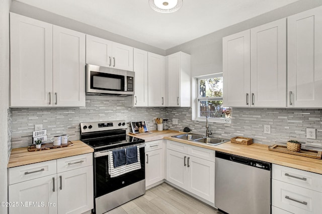 kitchen with wood counters, sink, white cabinetry, stainless steel appliances, and backsplash