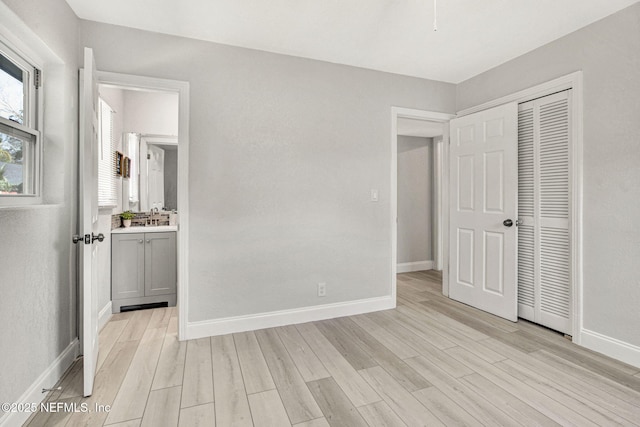 unfurnished bedroom featuring connected bathroom, sink, light hardwood / wood-style flooring, and a closet