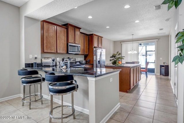 kitchen featuring a textured ceiling, hanging light fixtures, light tile patterned floors, appliances with stainless steel finishes, and kitchen peninsula