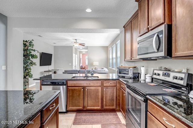 kitchen with appliances with stainless steel finishes, sink, dark stone countertops, light tile patterned floors, and a textured ceiling