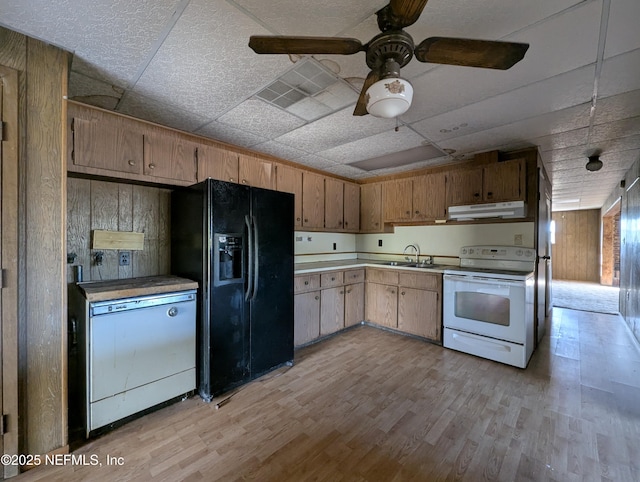 kitchen with sink, wooden walls, white appliances, light wood-type flooring, and a paneled ceiling