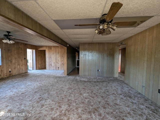 unfurnished room featuring ceiling fan, wood walls, and carpet flooring