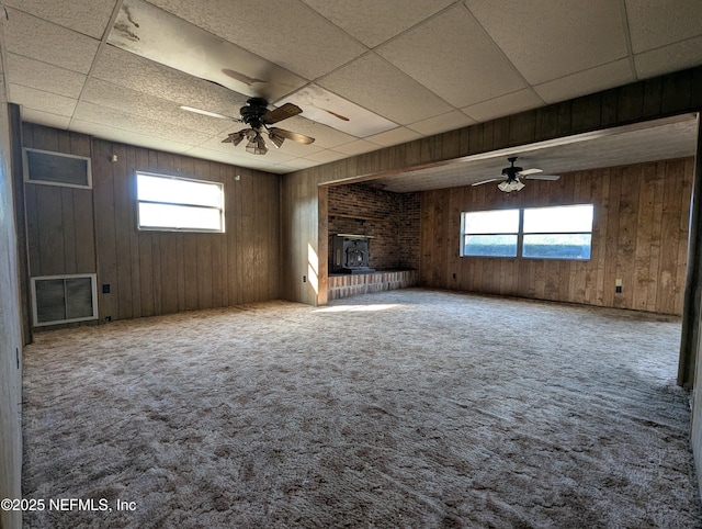 unfurnished living room with ceiling fan, a healthy amount of sunlight, carpet, and a wood stove