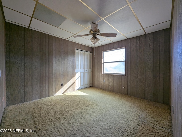 empty room featuring ceiling fan, carpet, and wooden walls