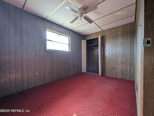 carpeted empty room featuring ceiling fan and wood walls