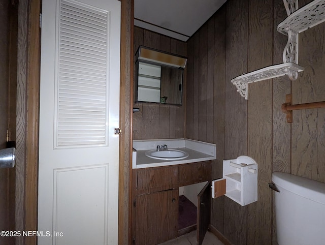 bathroom with toilet, vanity, and wooden walls