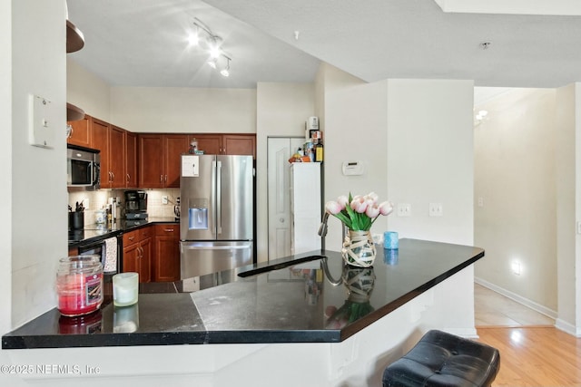 kitchen with kitchen peninsula, appliances with stainless steel finishes, backsplash, light tile patterned floors, and a breakfast bar