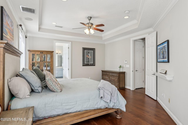 bedroom featuring crown molding, a tray ceiling, ensuite bath, and dark hardwood / wood-style floors