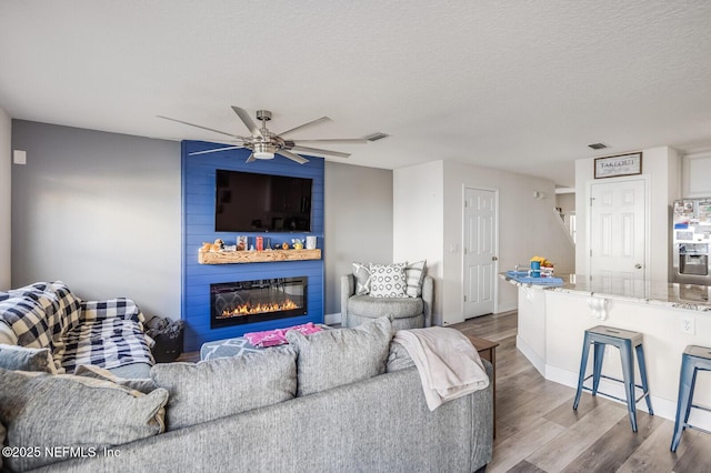 living room featuring ceiling fan, a fireplace, a textured ceiling, and light hardwood / wood-style floors