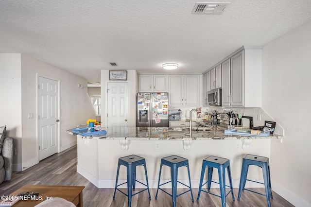 kitchen with kitchen peninsula, appliances with stainless steel finishes, a kitchen breakfast bar, and light stone counters