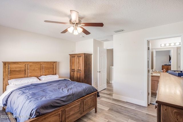 bedroom featuring ceiling fan, light hardwood / wood-style floors, ensuite bath, sink, and a textured ceiling