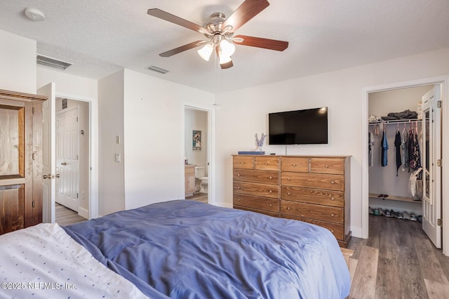 bedroom with hardwood / wood-style floors, a walk in closet, connected bathroom, a closet, and ceiling fan