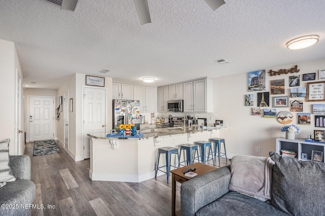 kitchen with white cabinetry, a kitchen bar, kitchen peninsula, stainless steel appliances, and light stone countertops