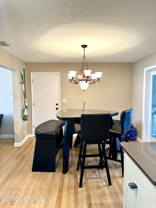 dining space featuring a textured ceiling, light hardwood / wood-style flooring, and a chandelier