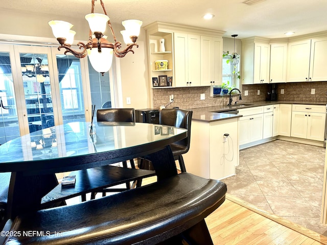 kitchen with decorative light fixtures, backsplash, sink, an inviting chandelier, and white cabinetry