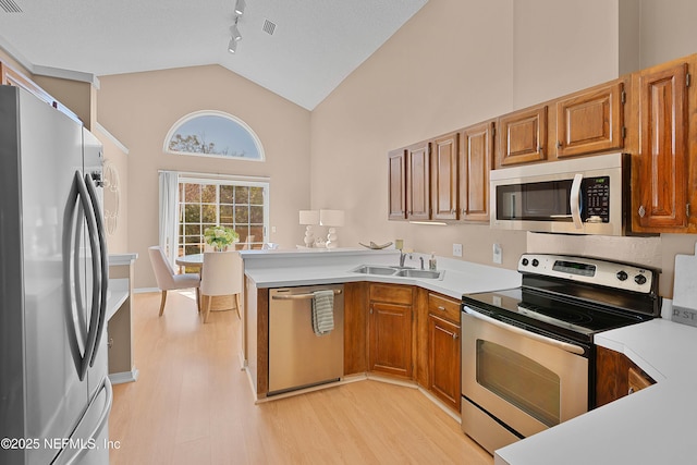 kitchen featuring sink, appliances with stainless steel finishes, high vaulted ceiling, kitchen peninsula, and light wood-type flooring