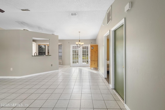 tiled empty room featuring a chandelier, a textured ceiling, and french doors