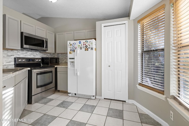 kitchen featuring light tile patterned floors, gray cabinets, stainless steel appliances, decorative backsplash, and lofted ceiling