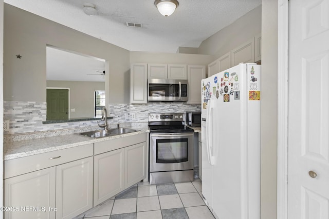 kitchen featuring ceiling fan, backsplash, sink, stainless steel appliances, and light tile patterned floors