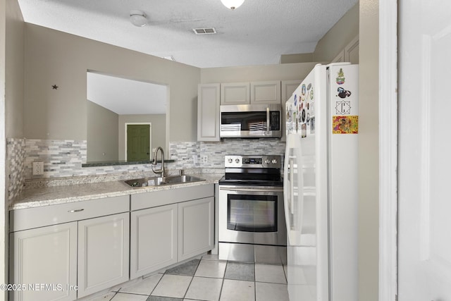 kitchen with a textured ceiling, appliances with stainless steel finishes, sink, backsplash, and light tile patterned floors