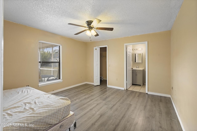 unfurnished bedroom featuring a textured ceiling, light hardwood / wood-style floors, sink, ceiling fan, and ensuite bathroom