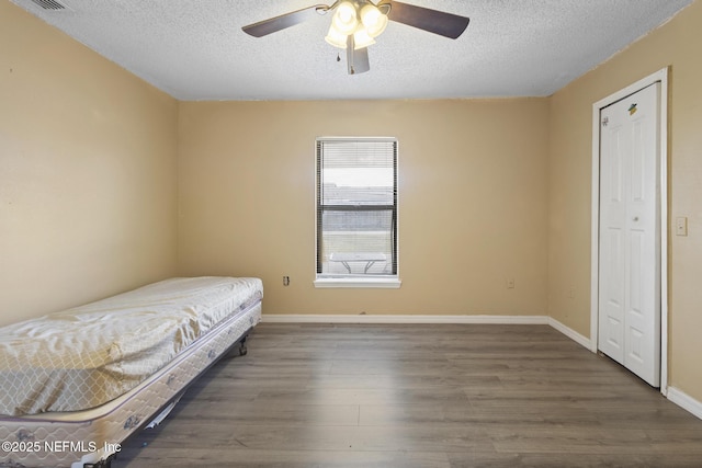 bedroom with ceiling fan, a textured ceiling, and dark hardwood / wood-style flooring