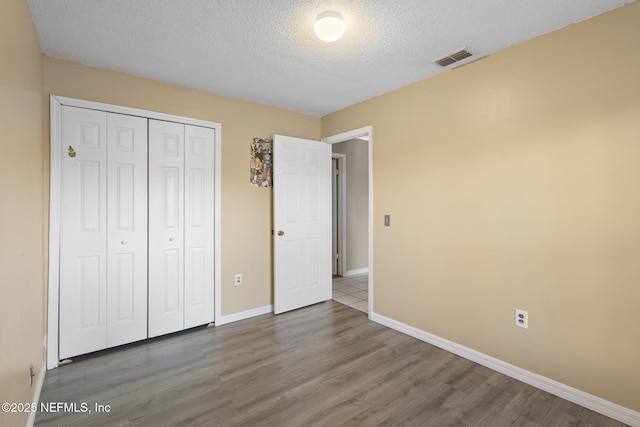 unfurnished bedroom with a textured ceiling, a closet, and hardwood / wood-style floors