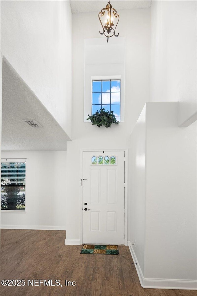 foyer with a high ceiling, wood finished floors, visible vents, and baseboards