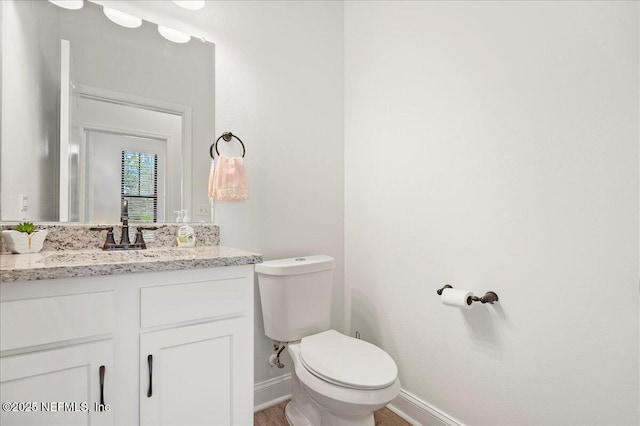 half bath featuring toilet, vanity, and baseboards