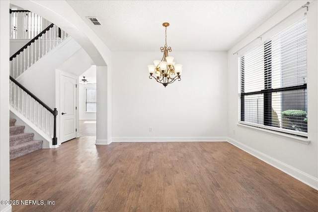 unfurnished room with visible vents, wood finished floors, stairway, arched walkways, and baseboards